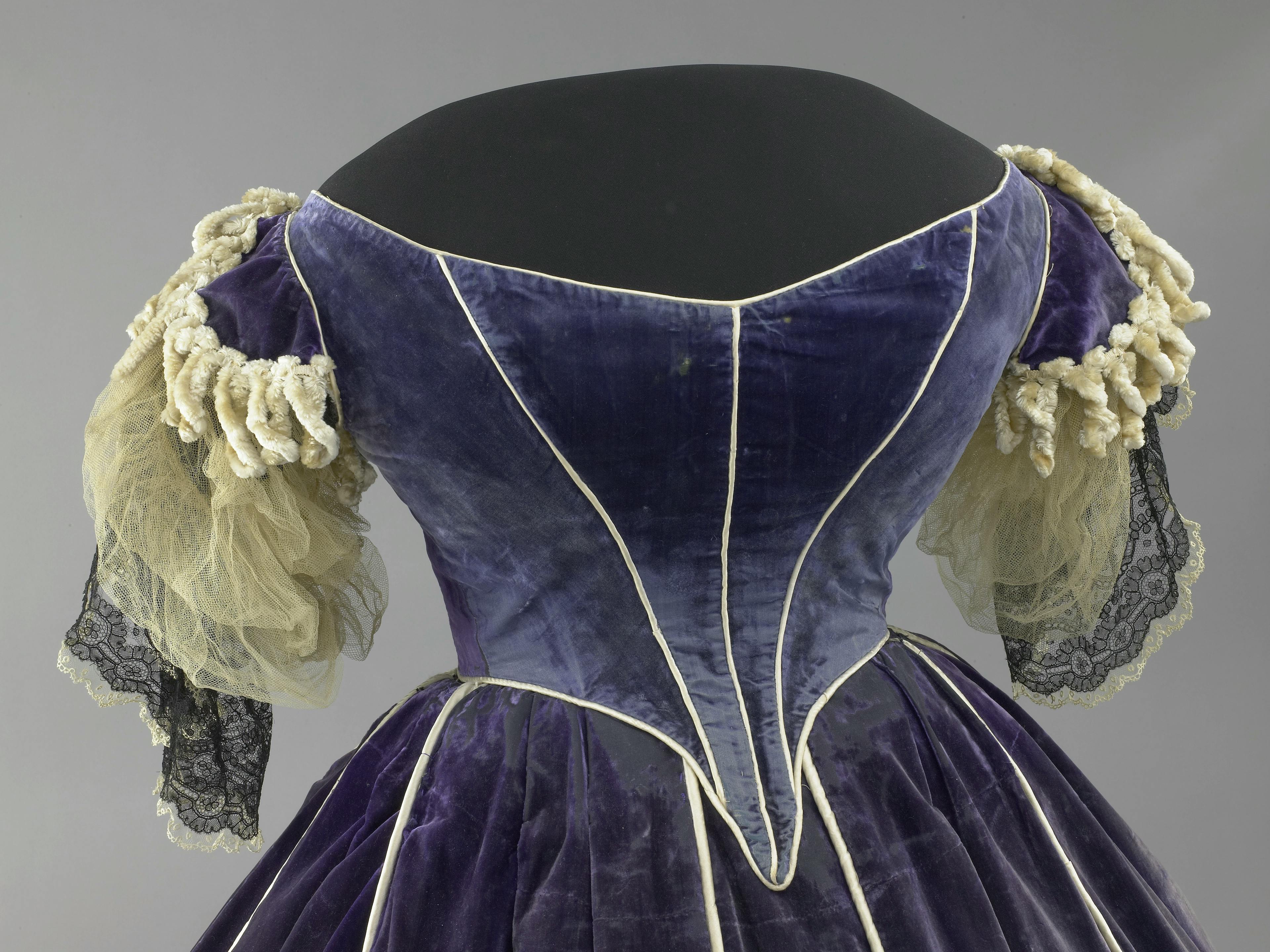 Close up of the back of a blue velvet gown with ruffles sleeves on a dressmaker's mannequin