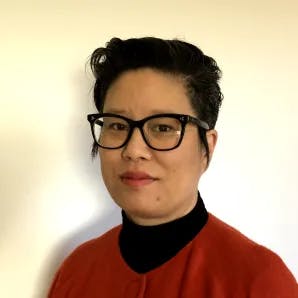 Headshot of Melissa Ho, a person with tan skin and short black hair wearing black-framed glasses, a black turtle neck, and a red sweater.